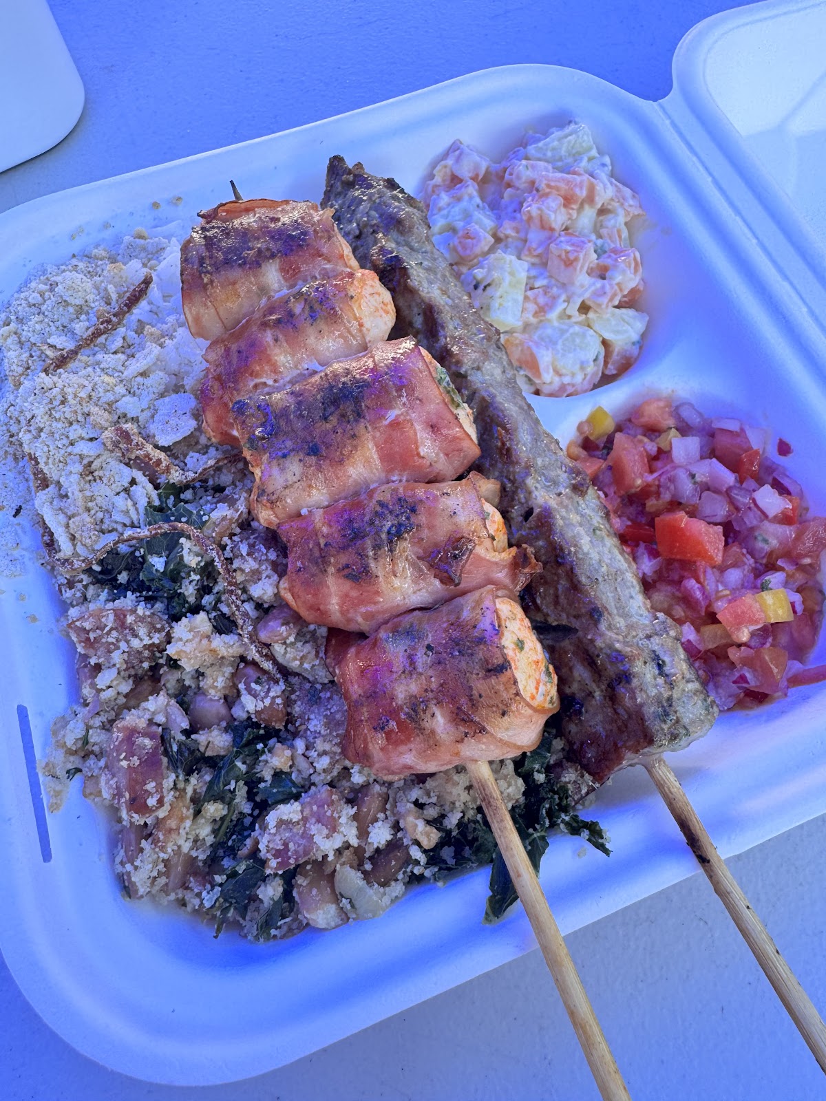 Chicken and bacon medalion skewer beside a sausage skewer over rice and greens