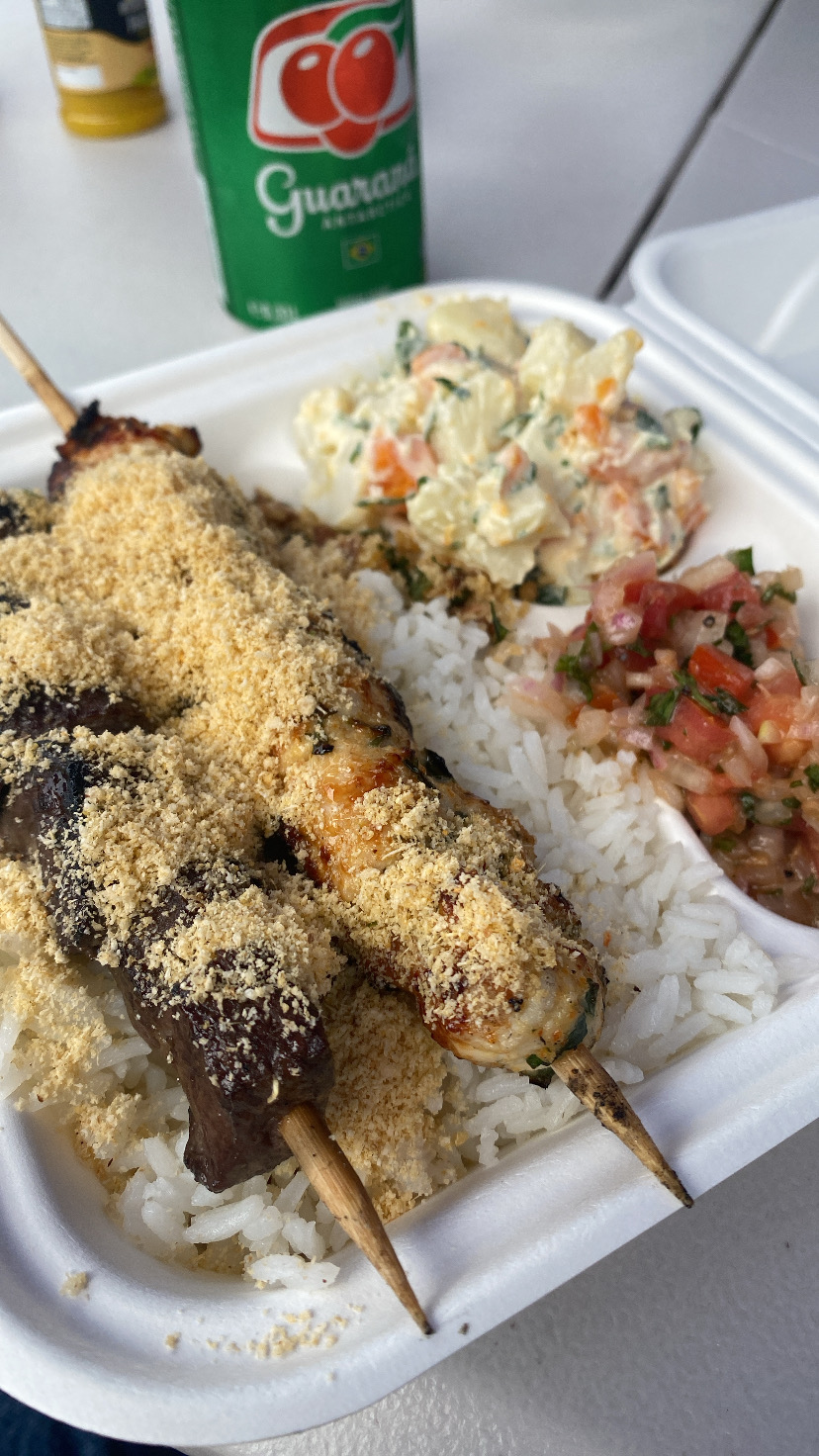 Skewers dusted with farofa over rice with a Guaraná can behind